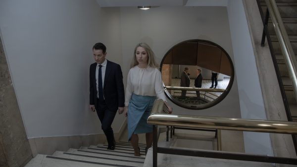 Άνδρας και γυναίκα με επίσημα ρούχα ανεβαίνουν σκάλες σε εσωτερικό χώρο.
