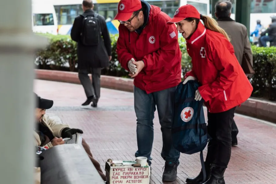 Εθελοντές του Ελληνικού Ερυθρού Σταυρού προσφέρουν βοήθεια σε άστεγο άνδρα στο δρόμο.