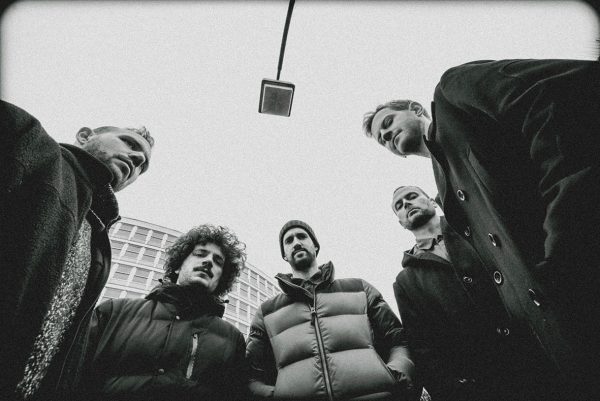 Πέντε άνδρες μέλη συγκροτήματος σε ασπρόμαυρη φωτογραφία από χαμηλή γωνία λήψης.