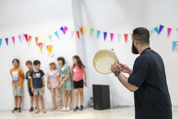 Παιδιά σε σειρά παρακολουθούν άνδρα που κρατάει κρουστό όργανο στο Summer Camp της Τεχνόπολης.