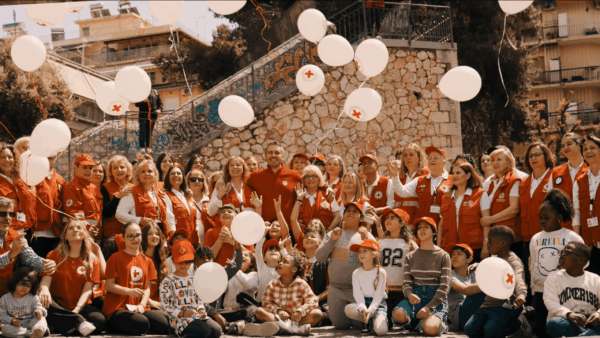 Ο Μιχάλης Χατζηγιάννης με εθελοντές και παιδιά του Ελληνικού Ερυθρού Σταυρού σε εορτασμό με λευκά μπαλόνια.