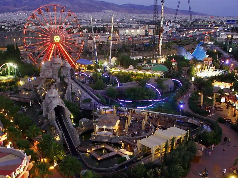 Πανοραμική νυχτερινή άποψη του Allou! Fun Park με τη φωτισμένη ρόδα και τα παιχνίδια.