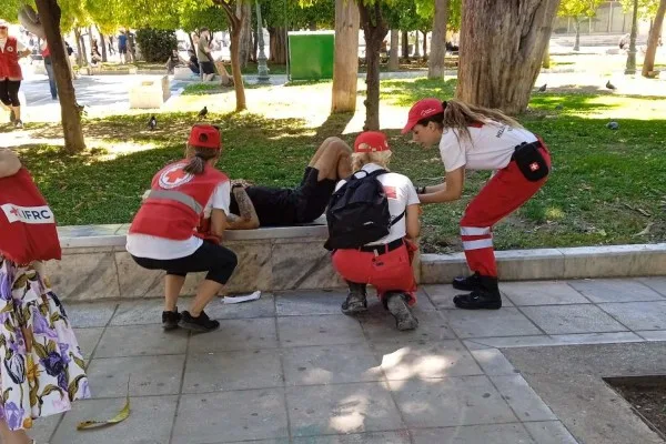 Εθελοντές του Ελληνικού Ερυθρού Σταυρού προσφέρουν βοήθεια σε άνδρα σε πάρκο κατά τη διάρκεια καύσωνα.