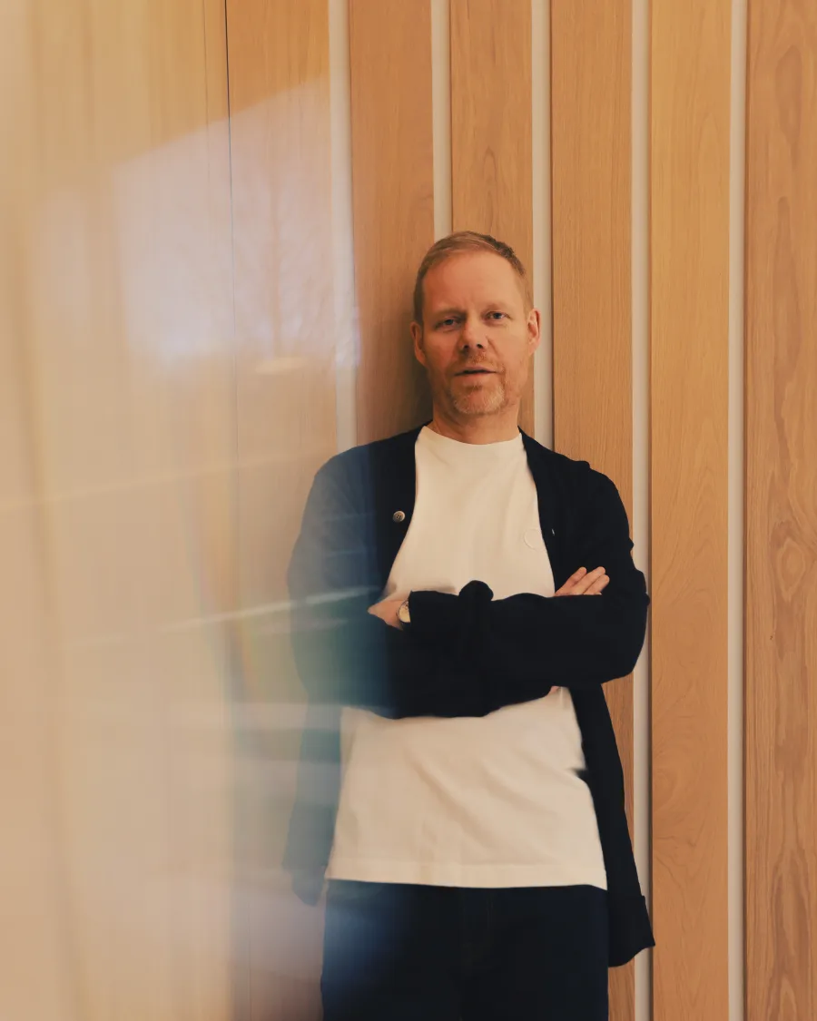 Ο Max Richter ποζάρει μπροστά από ξύλινη επένδυση τοίχου.