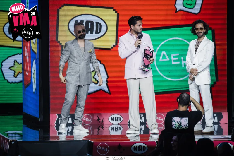 Τρεις άνδρες επί σκηνής στα Mad Video Music Awards 2025 από τη ΔΕΗ, με τον έναν να κρατάει βραβείο.