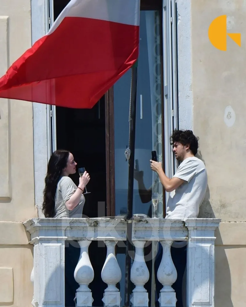 Η Billie Eilish και ο Nat Wolff ανταλλάσσουν ένα φιλί σε μπαλκόνι στη Βενετία.