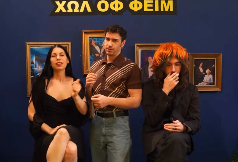 Τρεις παρουσιαστές σε στούντιο με μπλε φόντο και κάδρα.
