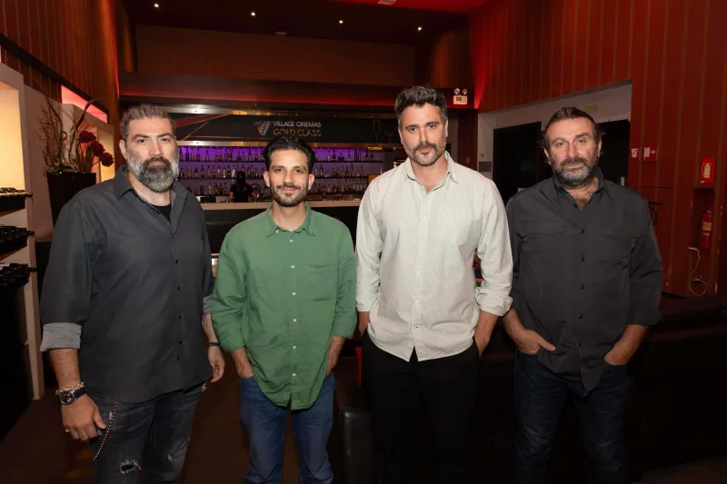 Τέσσερις άνδρες ποζάρουν σε εσωτερικό χώρο με μπαρ στο βάθος.