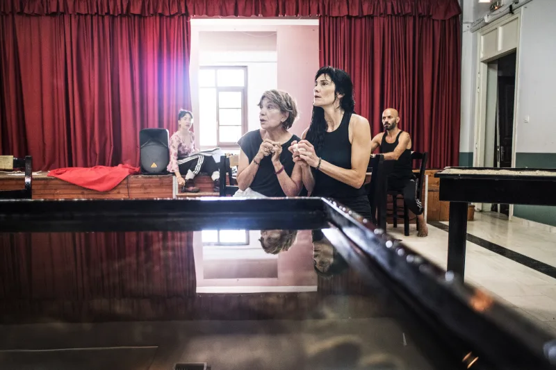Στιγμιότυπο από πρόβες για την παράσταση «Θήβα μοναξιά» σε εσωτερικό χώρο με κόκκινες κουρτίνες.
