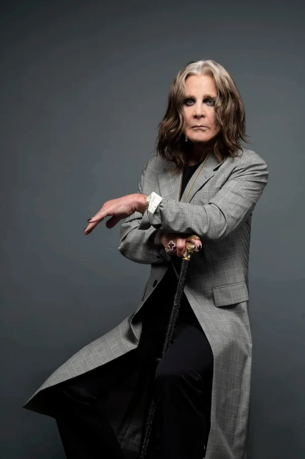 Ο Ozzy Osbourne ποζάρει με γκρι καρό παλτό και μπαστούνι.