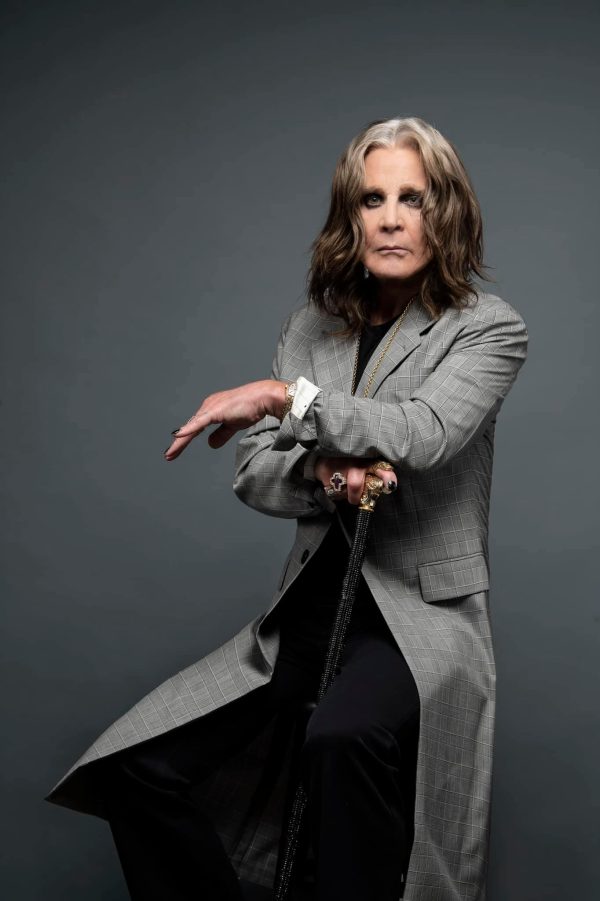 Ο Ozzy Osbourne ποζάρει με γκρι καρό παλτό και μπαστούνι.