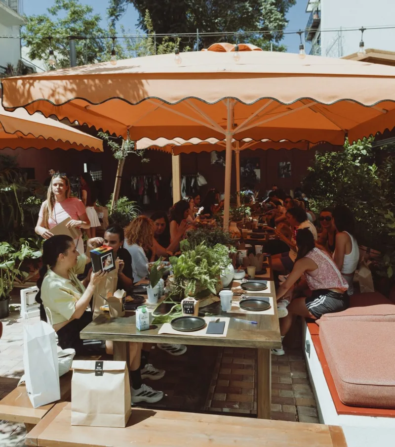 Ομάδα ατόμων σε brunch της adidas κάτω από μεγάλες πορτοκαλί ομπρέλες.