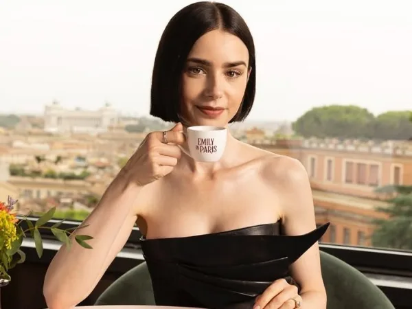 Η Lily Collins κρατά φλιτζάνι καφέ με το λογότυπο "Emily in Paris", απαντώντας αινιγματικά στην ερώτηση για την παρουσία της στην Ελλάδα.