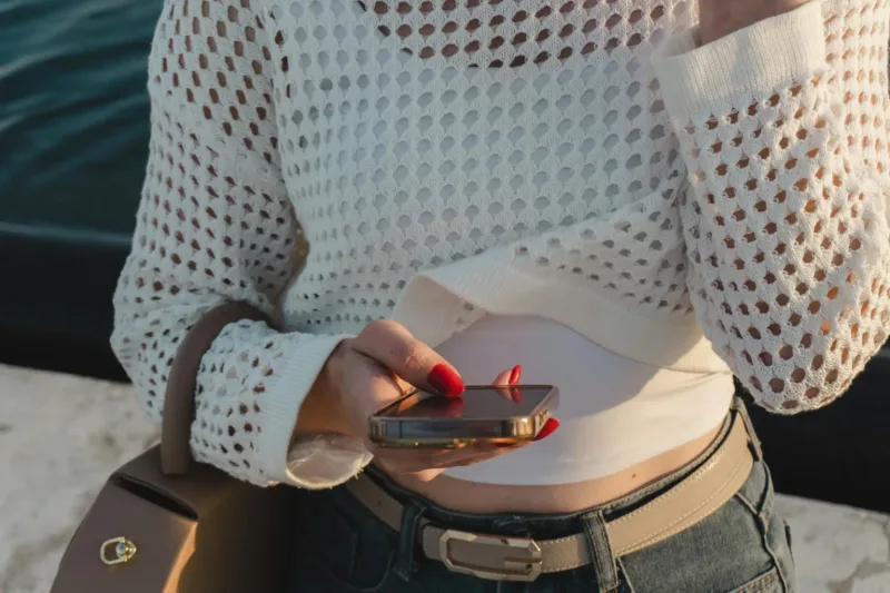 Γυναίκα που κρατάει smartphone και φοράει λευκό πλεκτό τοπ.