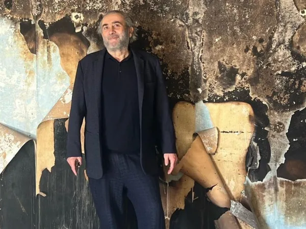 Ο Γιάννης Ζουγανέλης, ένας από τους Έλληνες celebrities, ποζάρει μπροστά από έναν τοίχο με ξεφλουδισμένη ταπετσαρία.