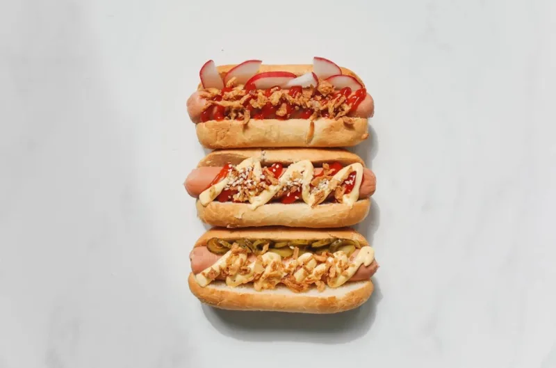 Τρία hot dogs με διαφορετικά toppings σε λευκό φόντο.