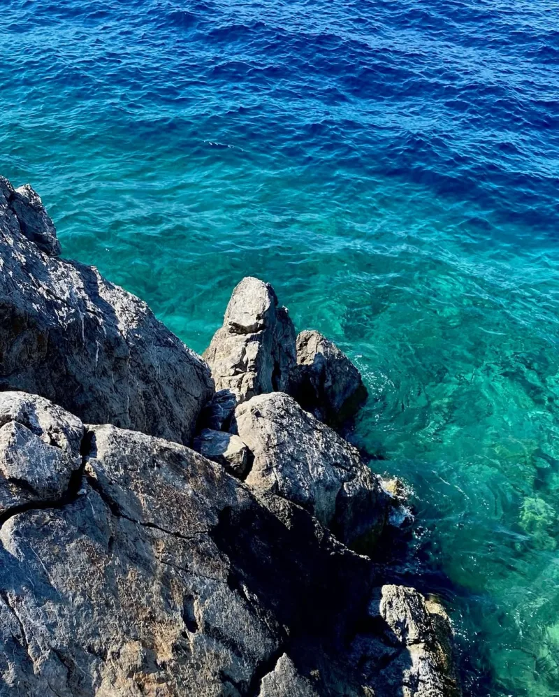 Βραχώδης ακτή με κρυστάλλινα γαλαζοπράσινα νερά στην Ελλάδα.