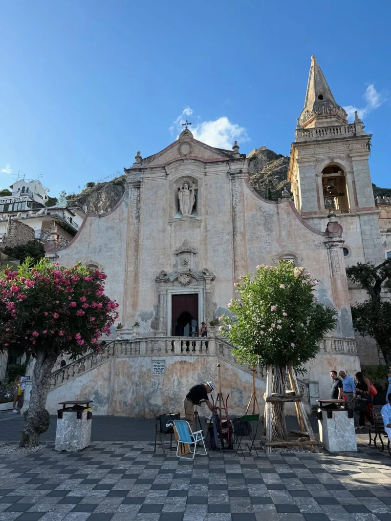 Εκκλησία σε πλατεία με ασπρόμαυρο δάπεδο και ανθισμένα δέντρα.