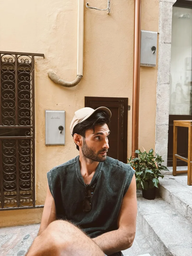 Άνδρας με αμάνικη μπλούζα και καπέλο κάθεται σε εξωτερικό χώρο.