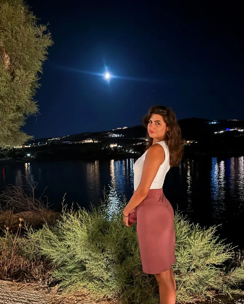 Γυναίκα ποζάρει μπροστά από θάλασσα τη νύχτα με φόντο το φεγγάρι.