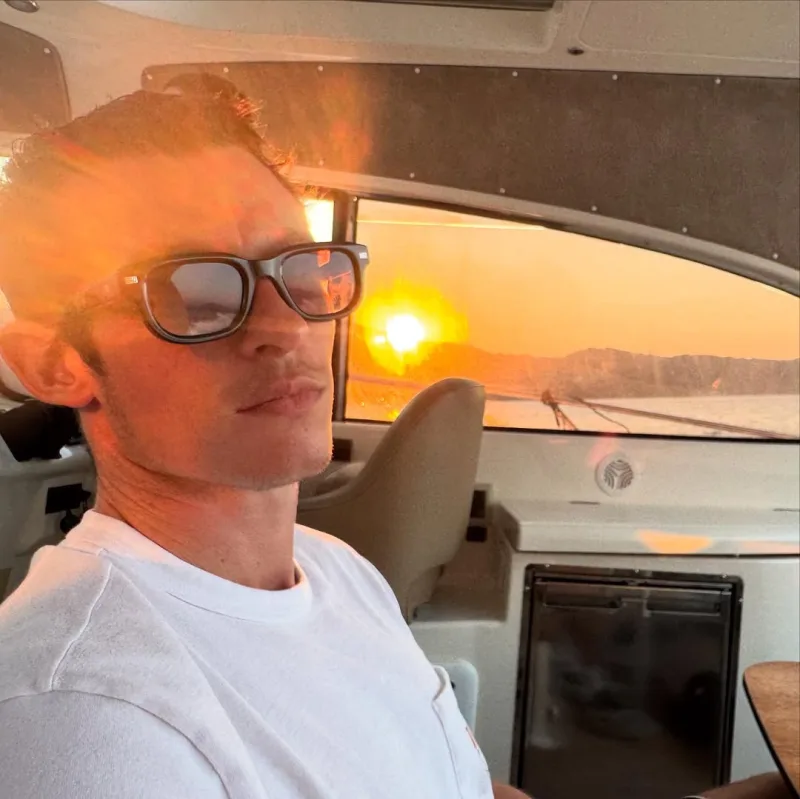 Ο Callum Turner με γυαλιά ηλίου μέσα σε σκάφος κατά τη διάρκεια του ηλιοβασιλέματος.