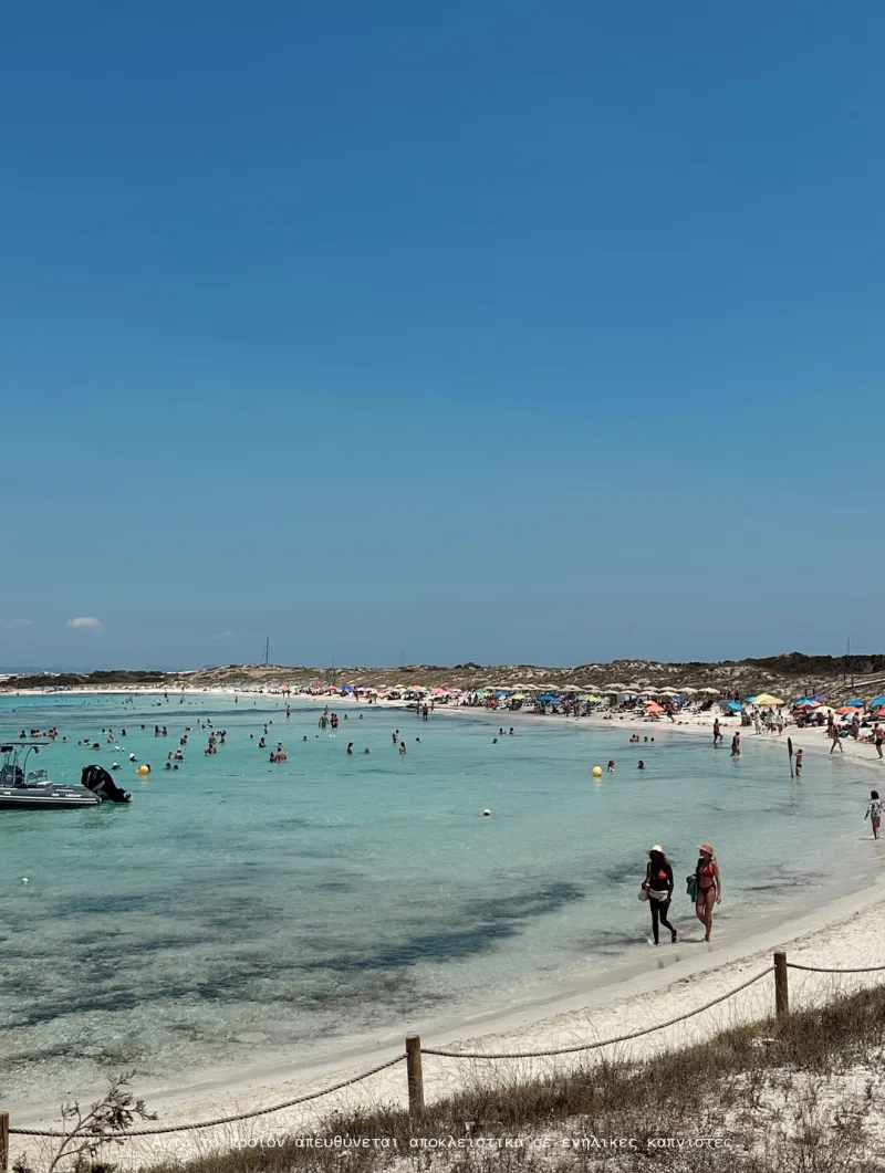 Παραλία με γαλαζοπράσινα νερά και κόσμο στην Ίμπιζα.