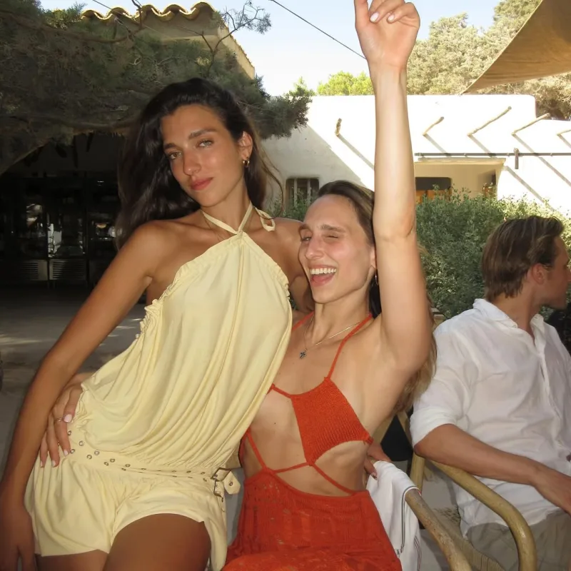 Η Dua Lipa με κίτρινο σύνολο ποζάρει δίπλα σε φίλη της σε εξωτερικό χώρο.