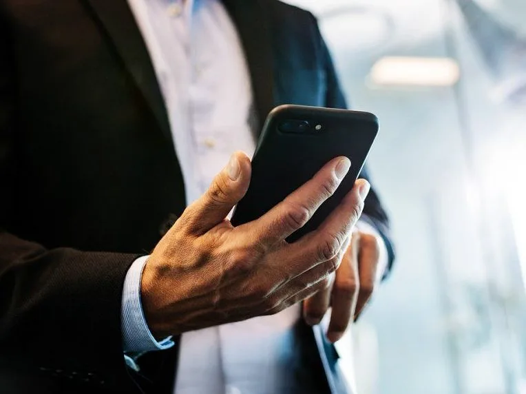 Άνδρας με κοστούμι κρατάει ένα μαύρο smartphone.