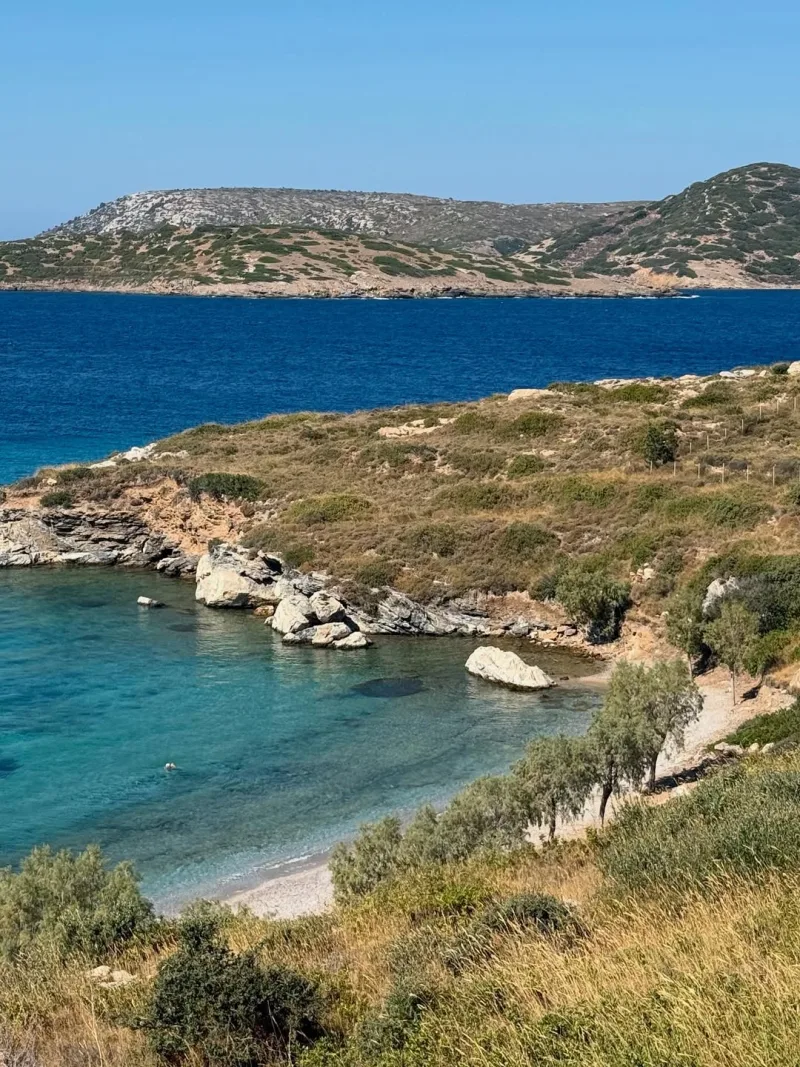 Πανοραμική θέα μιας απομονωμένης παραλίας με γαλαζοπράσινα νερά και βραχώδη ακτογραμμή.