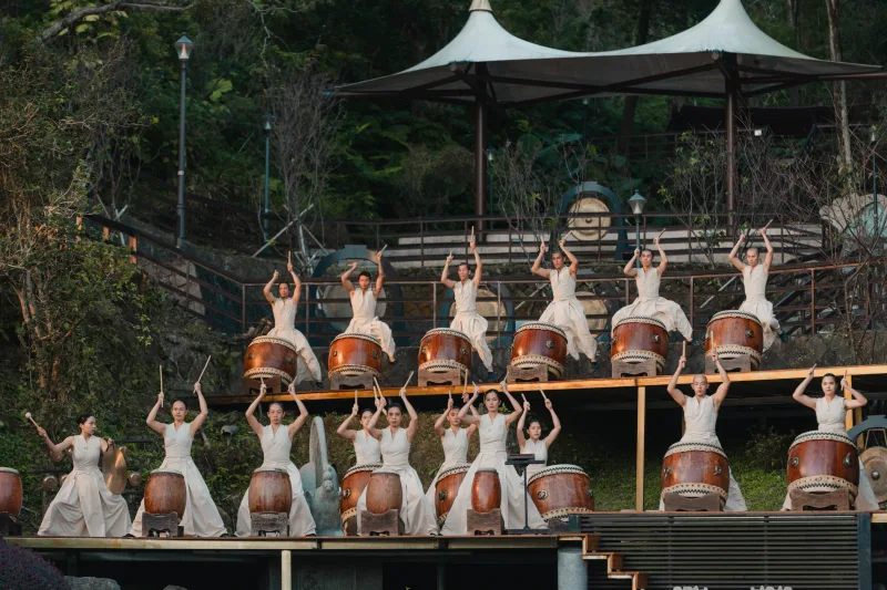 Μέλη των U-Theatre παίζουν τύμπανα σε υπαίθρια σκηνή.