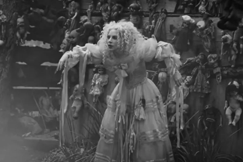 Η Lady Gaga σε ασπρόμαυρο πλάνο από το βίντεο κλιπ Dead Dance, περιτριγυρισμένη από κρεμασμένες κούκλες.