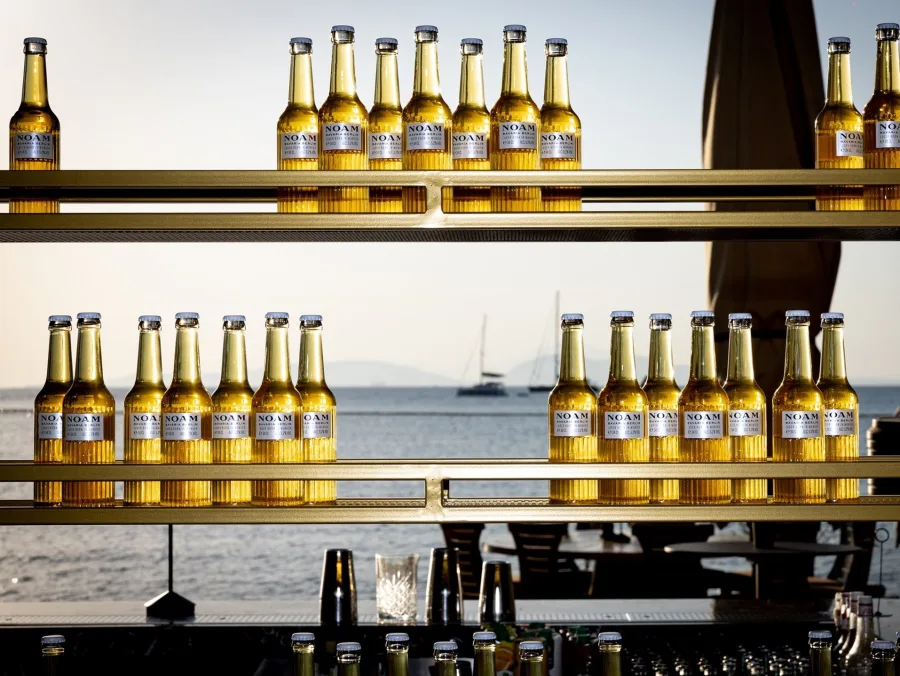 Η premium lager μπίρα NOAM σε εμβληματική φιάλη με φόντο το ελληνικό ηλιοβασίλεμα.