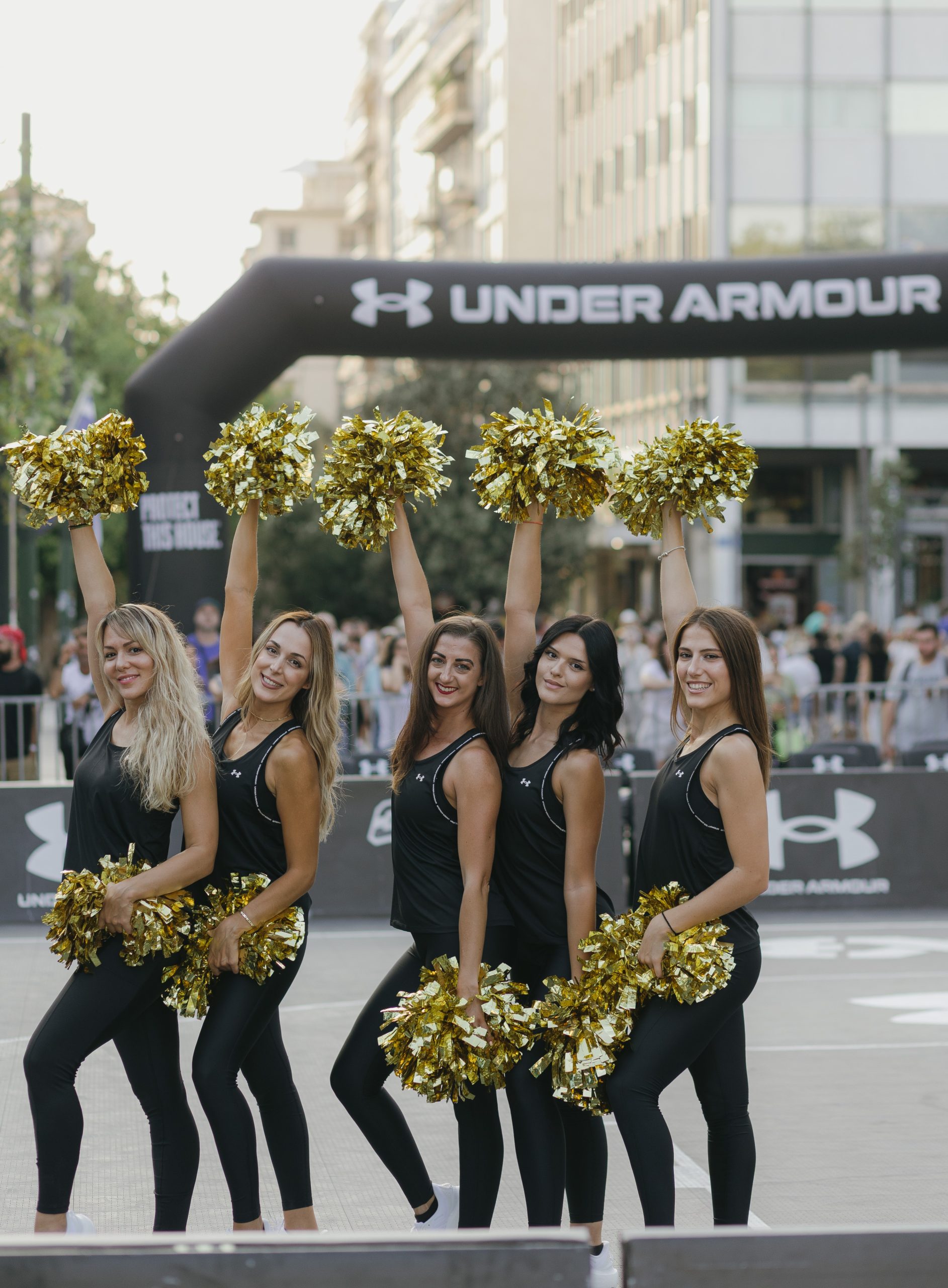 Πέντε cheerleaders με χρυσά pom-poms σε εκδήλωση της Under Armour.