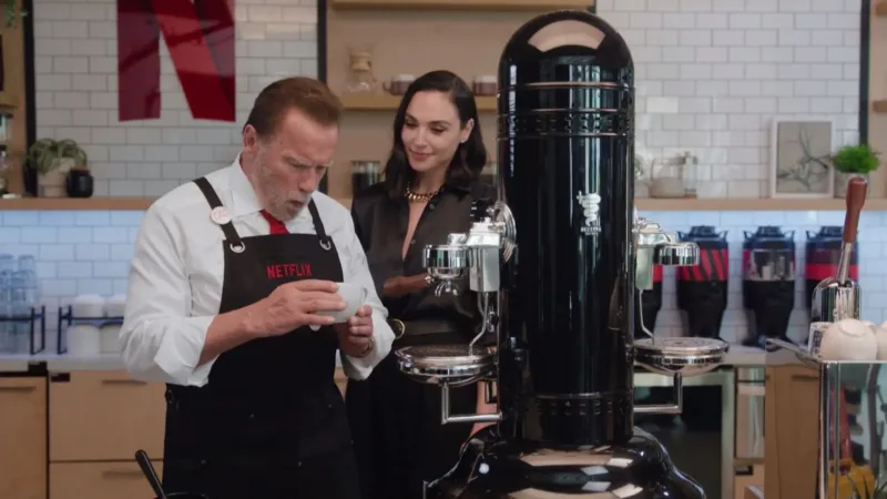 Ο Arnold Schwarzenegger και η Gal Gadot δίπλα σε μια μεγάλη μηχανή καφέ.