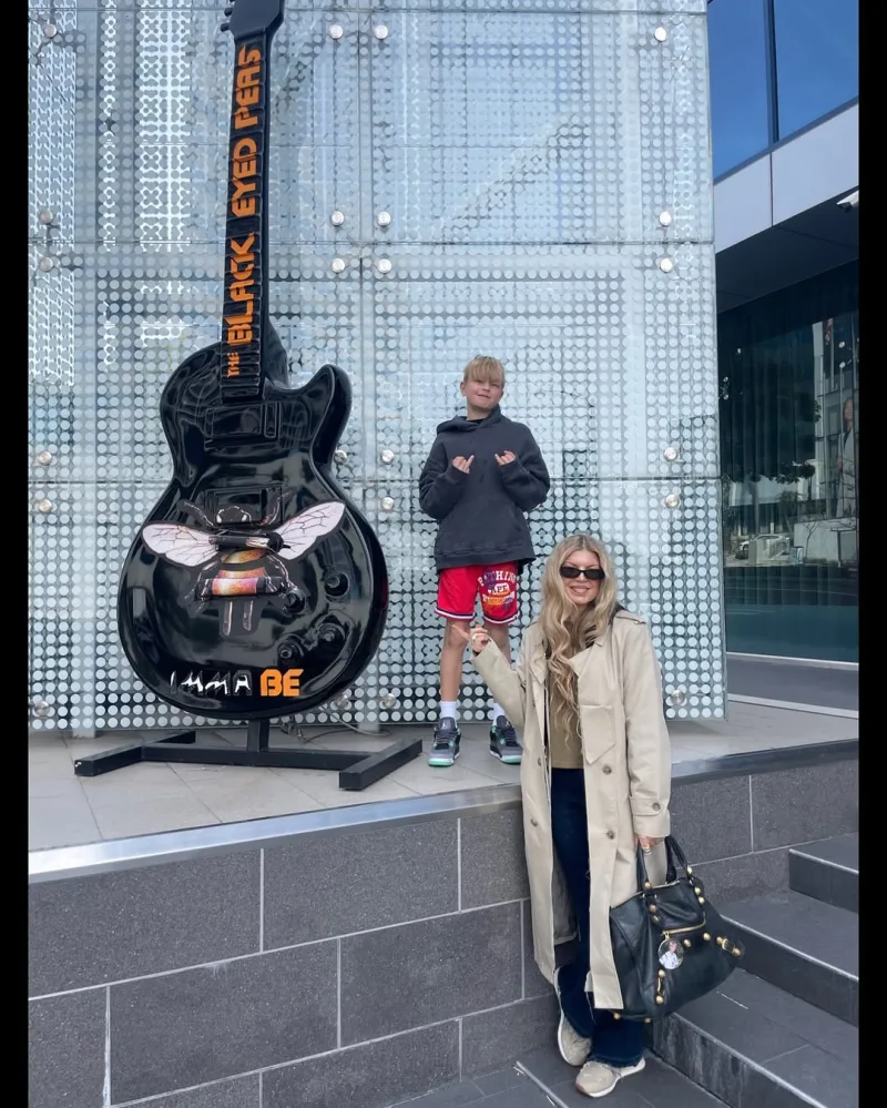 Η Fergie με τον γιο της Axl δίπλα σε μια μεγάλη μαύρη κιθάρα των Black Eyed Peas.