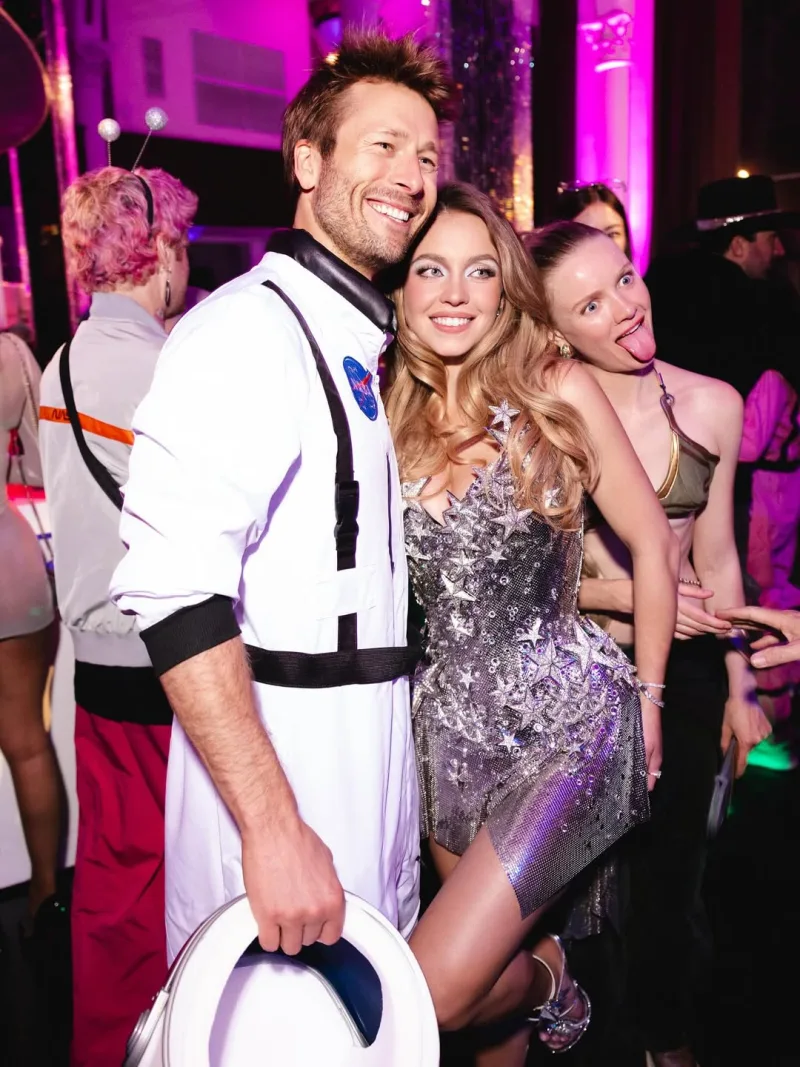 Η Sydney Sweeney με ασημί φόρεμα και ο Glen Powell ως αστροναύτης σε πάρτι.