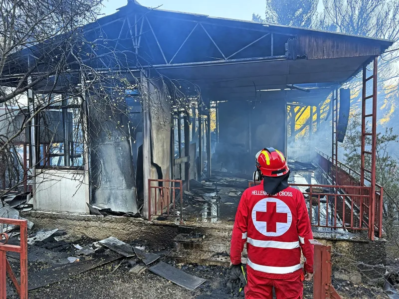 Εθελοντής του Ελληνικού Ερυθρού Σταυρού μπροστά από καμένο κτίριο.