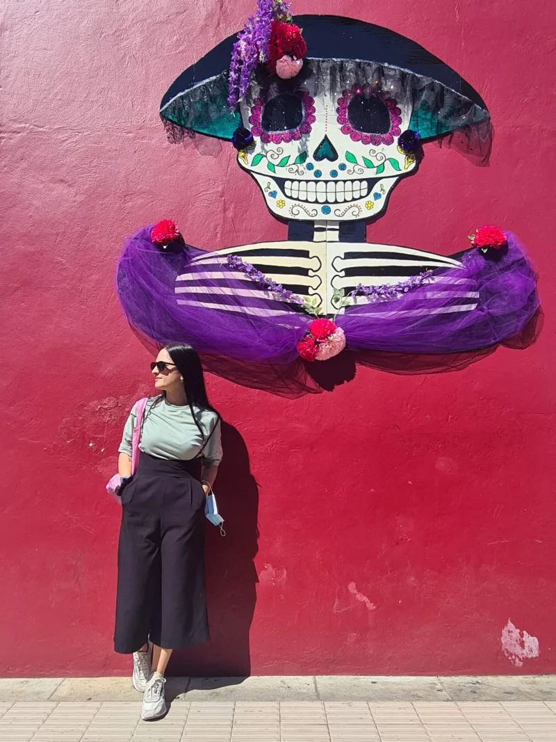 Γυναίκα μπροστά από τοιχογραφία σκελετού Catrina για την Día de Muertos.