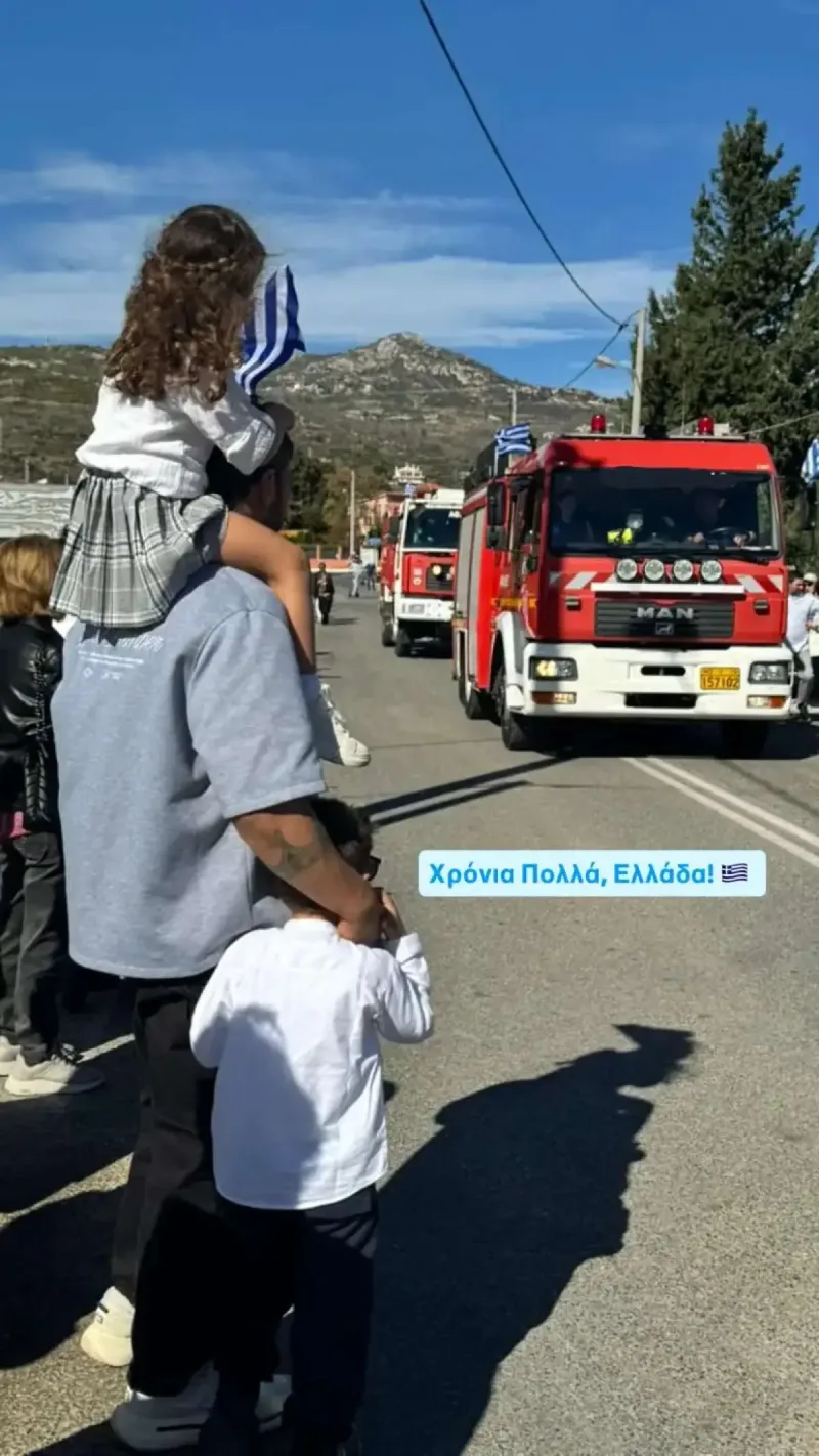 Άνδρας με δύο παιδιά παρακολουθεί παρέλαση πυροσβεστικών οχημάτων.