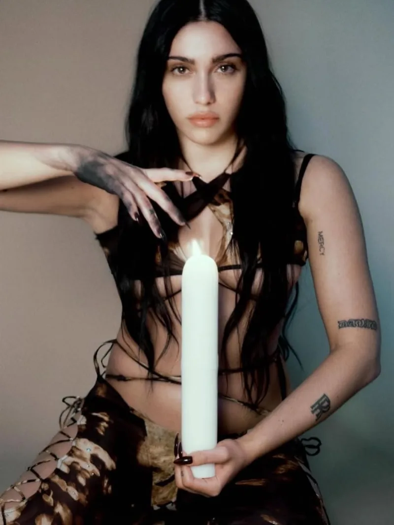 Η Lourdes Leon με σκούρα μαλλιά κρατάει ένα μεγάλο λευκό κερί.