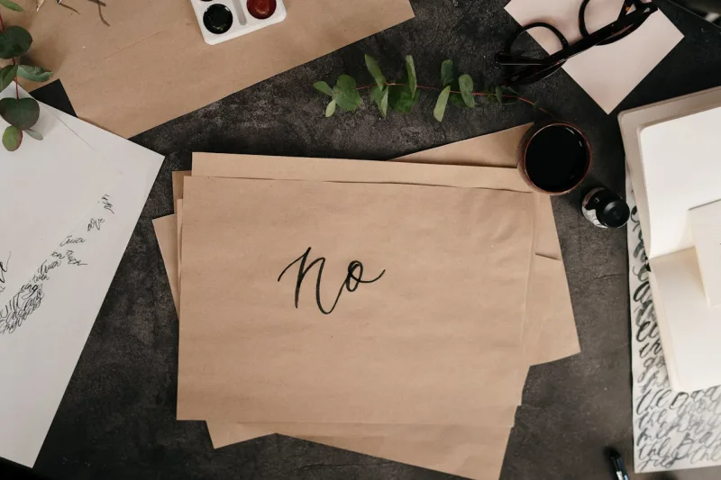 Χειρόγραφη λέξη «no» σε καφέ χαρτί πάνω σε γραφείο με σύνεργα καλλιγραφίας.