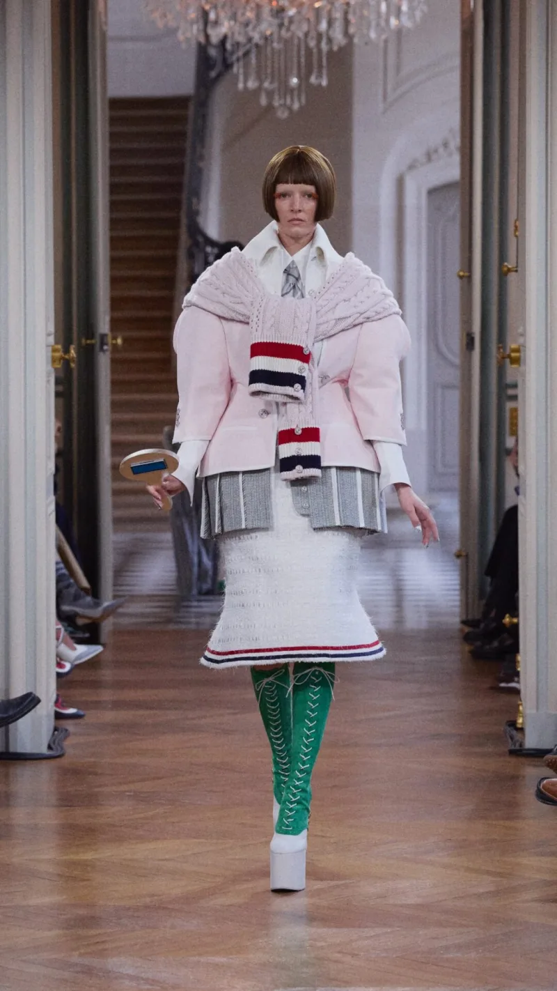 Μοντέλο στην επίδειξη Thom Browne SS26 με ροζ σακάκι και πλεκτή ζακέτα.