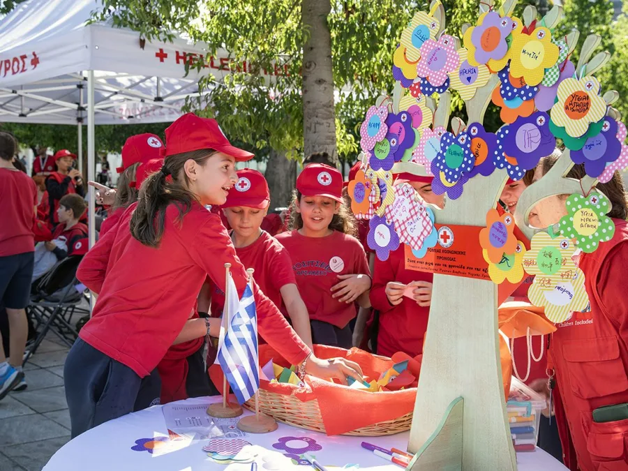 Παιδιά με κόκκινα μπλουζάκια και καπέλα του Ελληνικού Ερυθρού Σταυρού σε εκδήλωση.