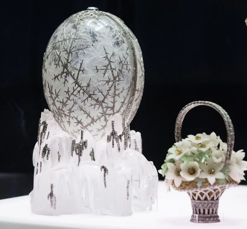 Το Χειμερινό Αυγό Fabergé του Τσάρου Νικόλαου Β’ πάνω σε κρυστάλλινη βάση δίπλα σε ένα μικρό καλάθι με λουλούδια.