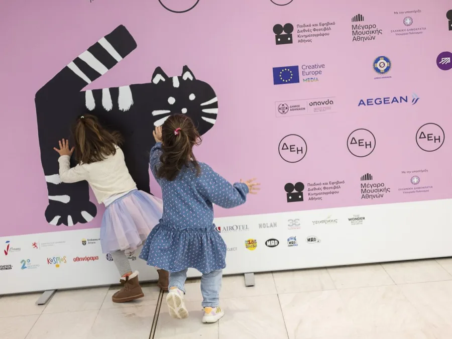Δύο μικρά κορίτσια μπροστά από αφίσα του Παιδικού και Εφηβικού Διεθνούς Φεστιβάλ Κινηματογράφου Αθήνας.