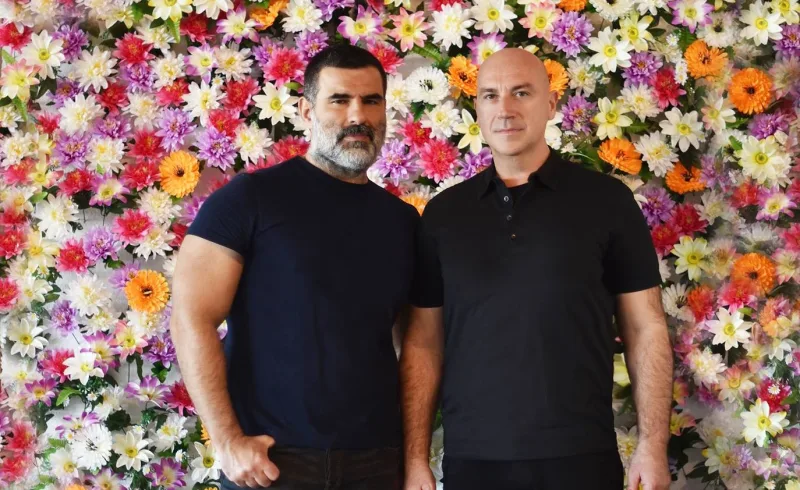 Οι Deux Hommes μπροστά από έναν τοίχο με πολύχρωμα λουλούδια.