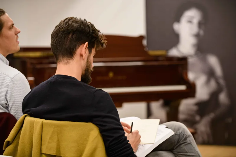 Συμμετέχων σε masterclass κρατά σημειώσεις μπροστά από ένα πιάνο και μια φωτογραφία της Μαρίας Κάλλας.