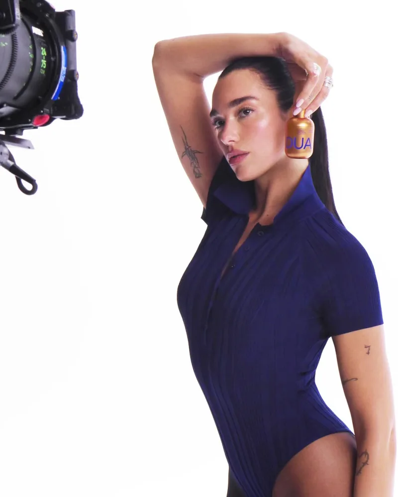 Η Dua Lipa ποζάρει κρατώντας ένα χρυσό μπουκάλι skincare.