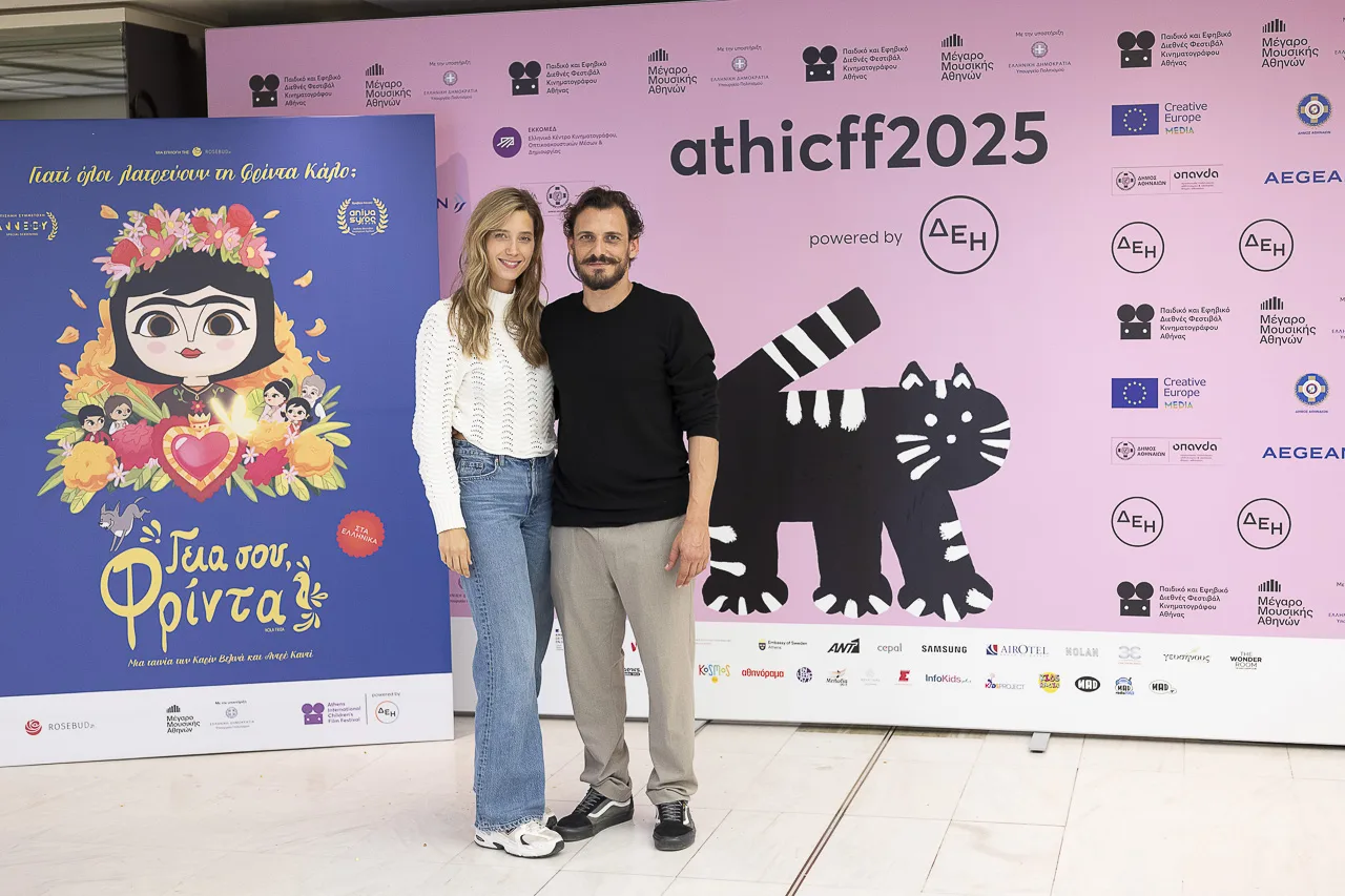 Ένας άνδρας και μια γυναίκα ποζάρουν μπροστά από το backdrop του Παιδικού και Εφηβικού Διεθνούς Φεστιβάλ Κινηματογράφου Αθήνας.