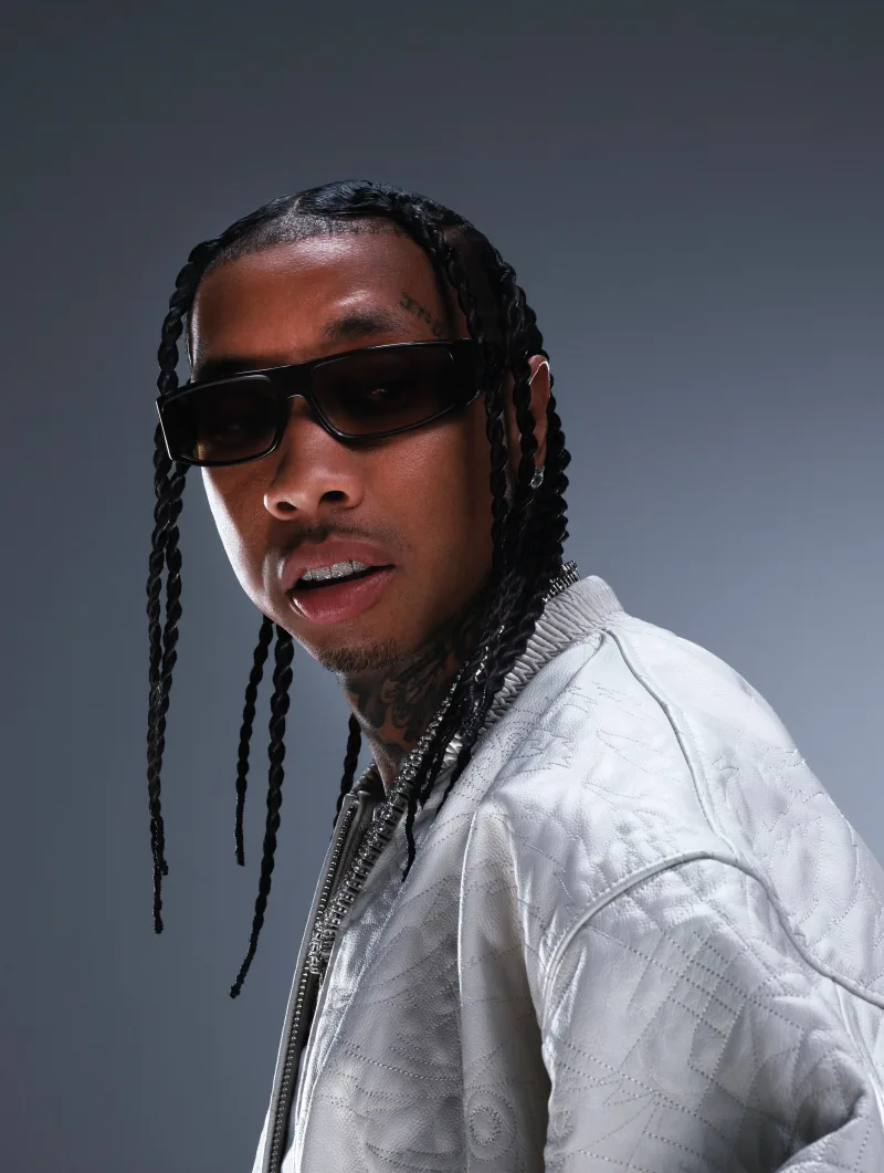 Ο Tyga με πλεξούδες, μαύρα γυαλιά ηλίου και λευκό μπουφάν.